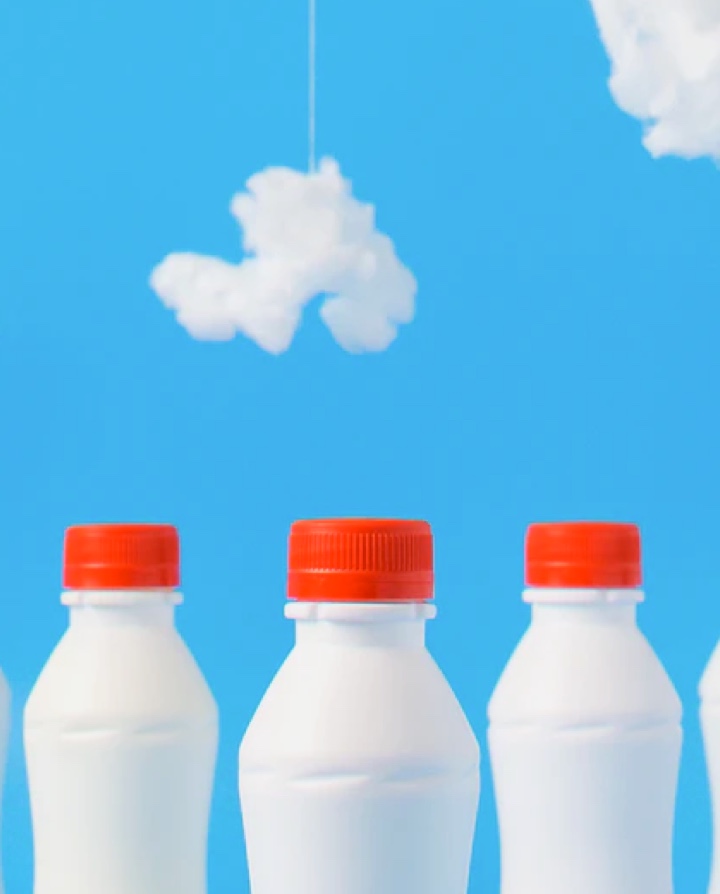 Picture presenting white bottles with milk ending with a red closure facing a painted sky