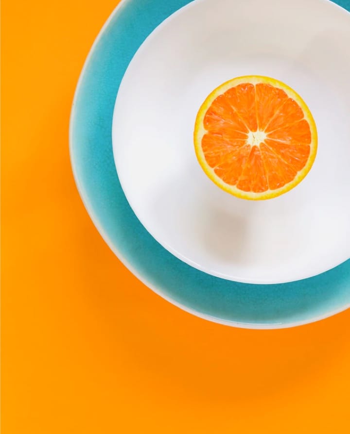 Picture of an orange in a white bowl with orange background