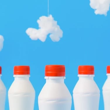 Picture presenting white bottles with milk ending with a red closure facing a painted sky