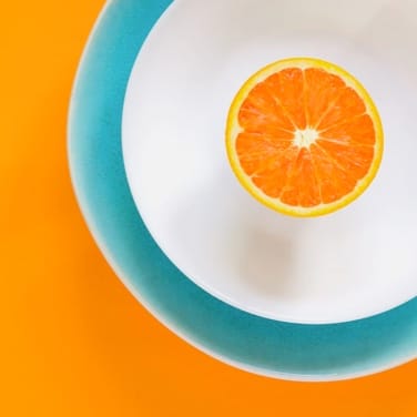 Picture of an orange in a white bowl with orange background